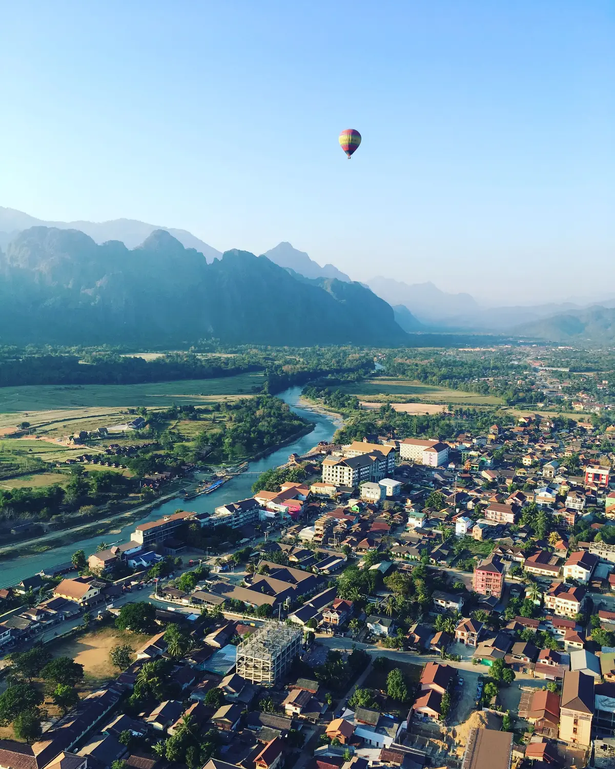 Hot air balloon floating over the town of Vang Vieng with a winding river and karst mountains in Laos.