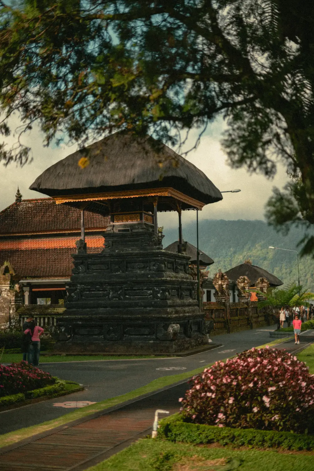 Traditional Balinese temple with a thatched roof set among gardens and misty mountains in Bali, Indonesia.