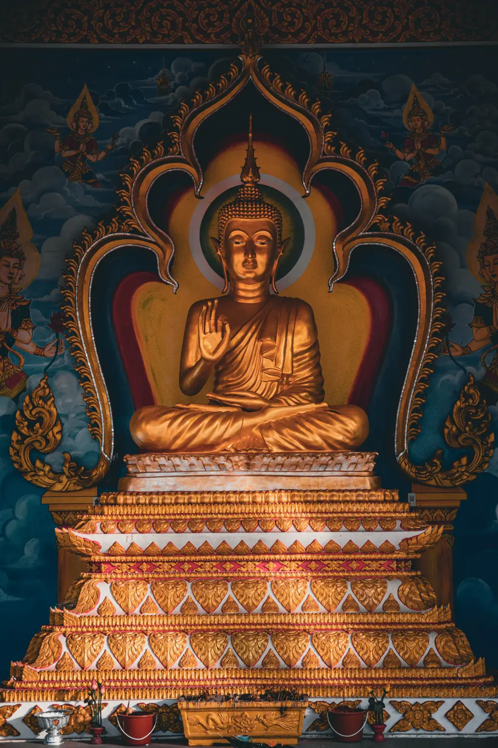 Golden seated Buddha statue on an elaborate gilded pedestal inside a temple in Laos.