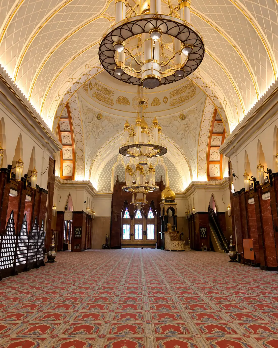 Opulent mosque prayer hall interior with ornate vaulted ceiling, golden chandeliers and patterned carpet, Brunei