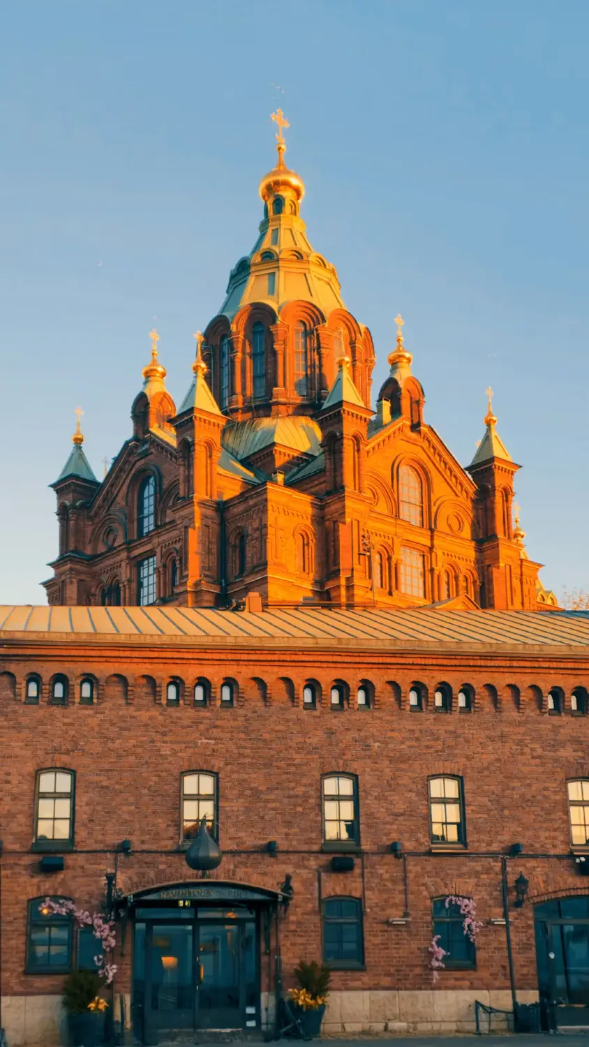 Red-brick cathedral with golden domes and crosses glowing in warm evening light behind a historic brick building.