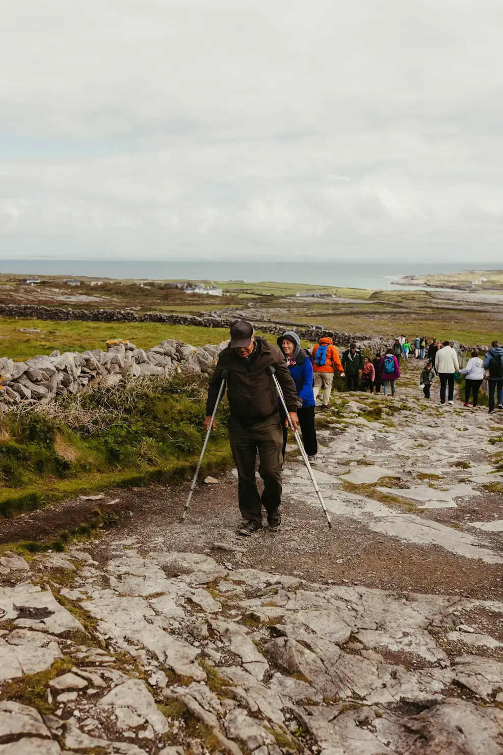 Hikers walking along a rocky, muddy trail across an open landscape, Ireland.