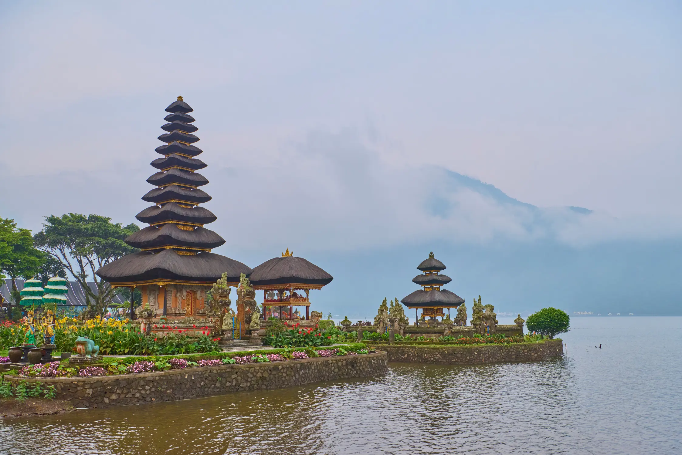 Balinese water temple Pura Ulun Danu Beratan with tiered pagoda towers on the shore of Lake Bratan, surrounded by mist-covered mountains in Bali, Indonesia.