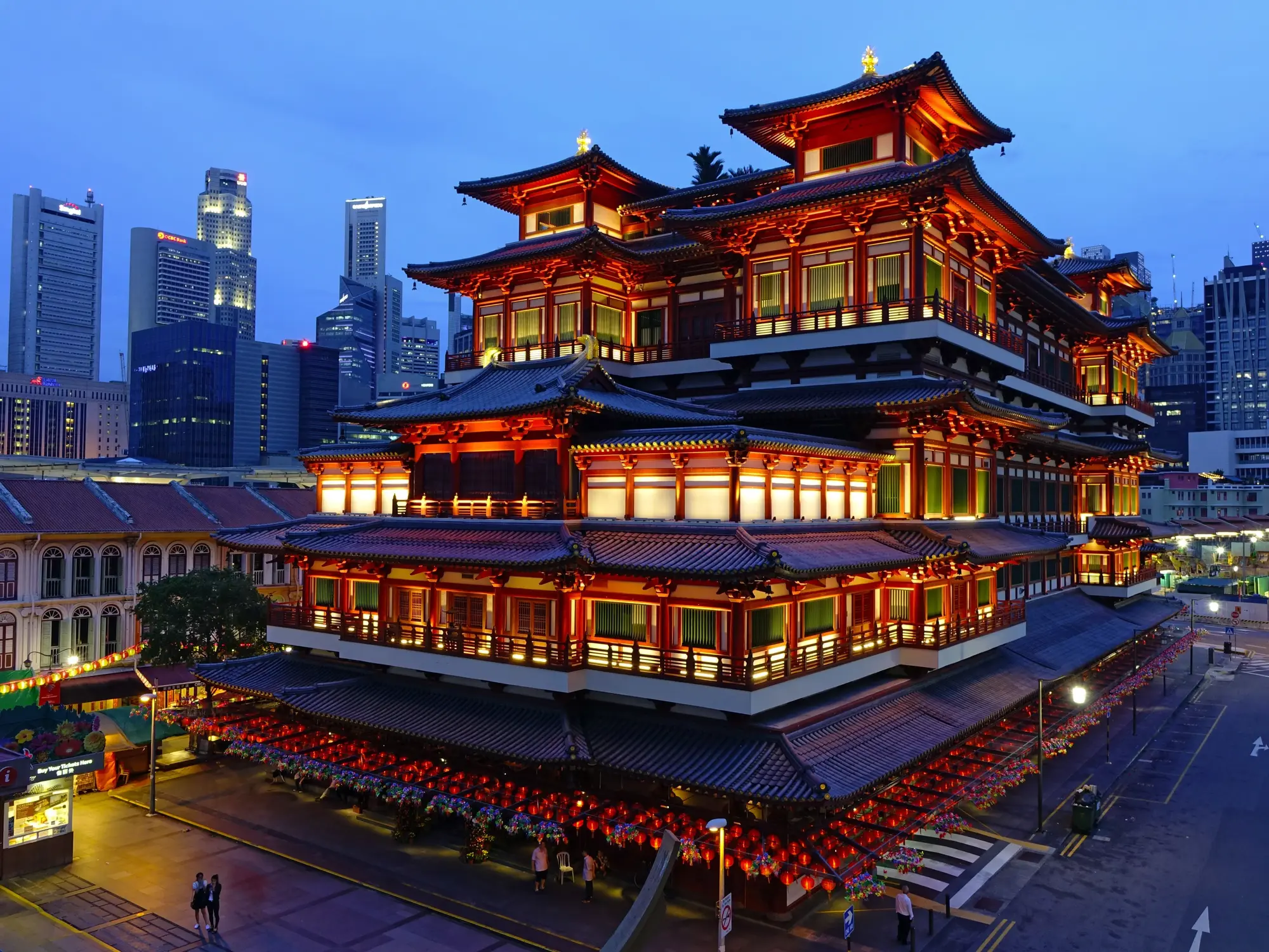 Buddha Tooth Relic Temple illuminated at blue hour dusk with Singapore CBD skyscrapers in background Chinatown