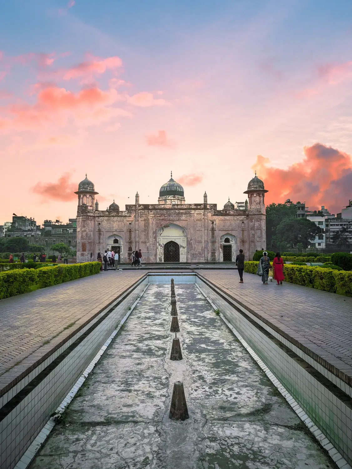Lalbagh Fort Mughal-era mausoleum of Bibi Pari at dramatic pink and orange sunset with garden pathway and visitors, Old Dhaka, Bangladesh