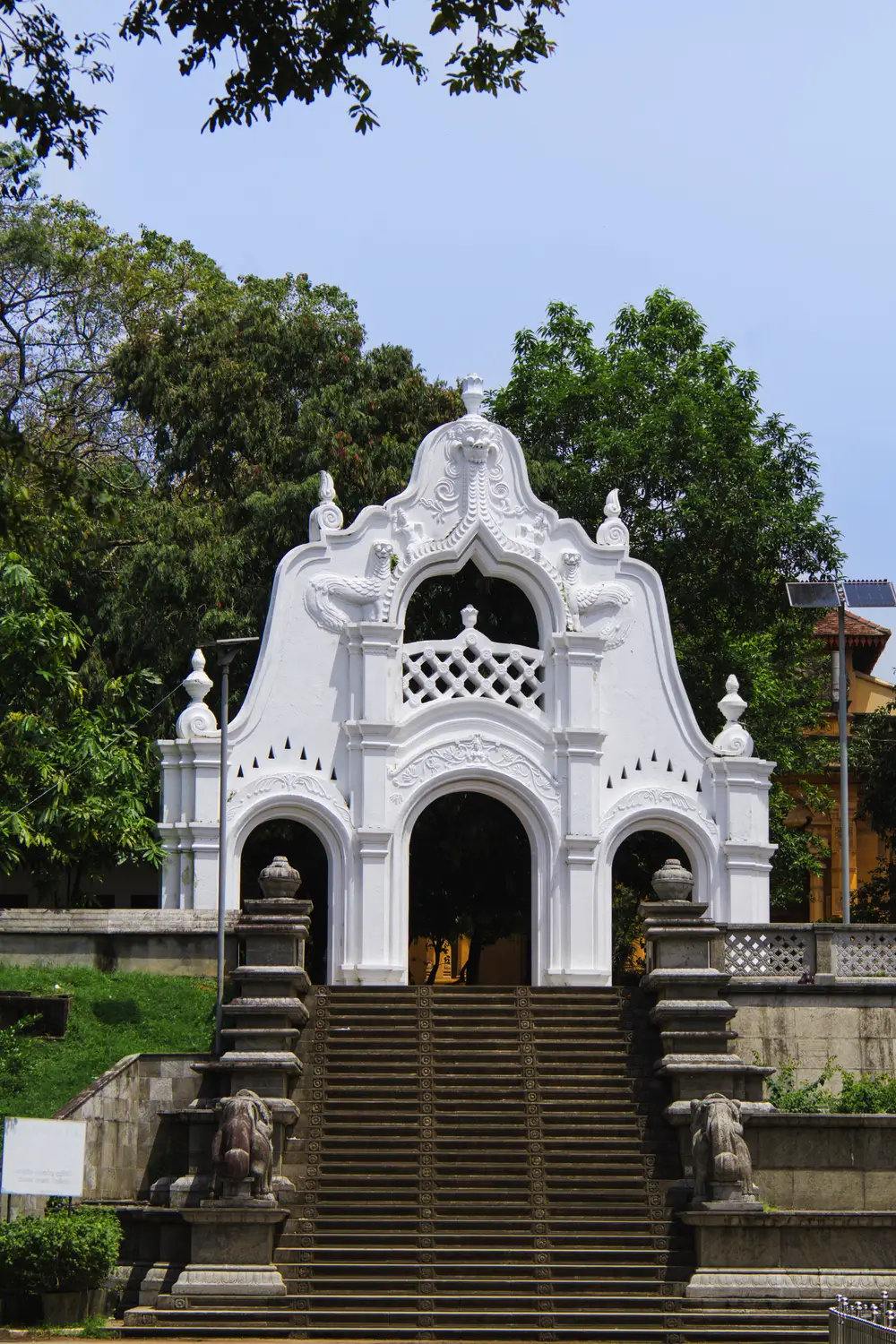 White colonial-style temple building with a decorative facade atop stone steps in Sri Lanka.