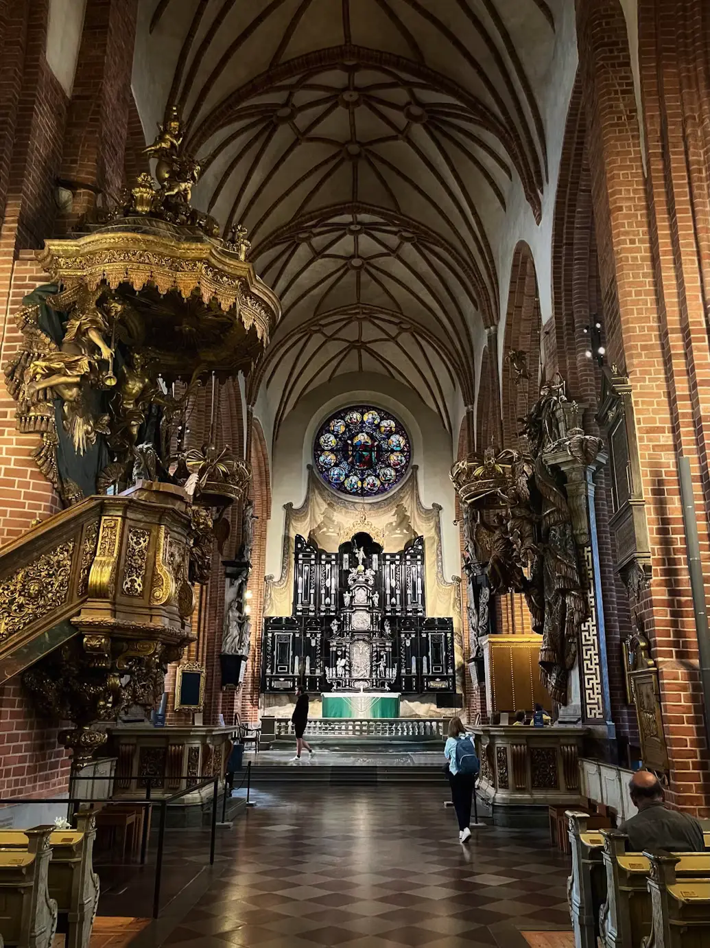 Ornate church interior with a vaulted ceiling, elaborate carved pulpit, and a person walking down the central aisle.