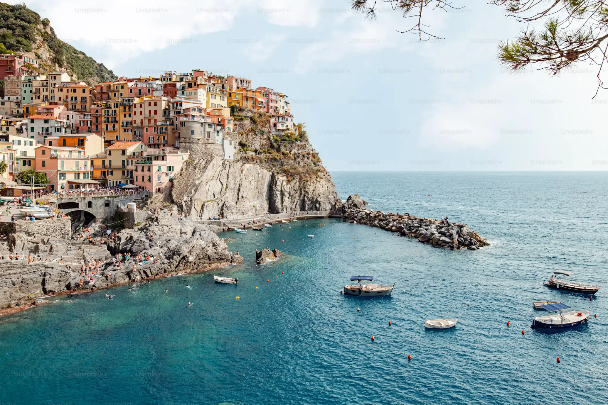 Manarola's colorful cliffside houses overlooking small boats anchored in the bay, Cinque Terre, Italy