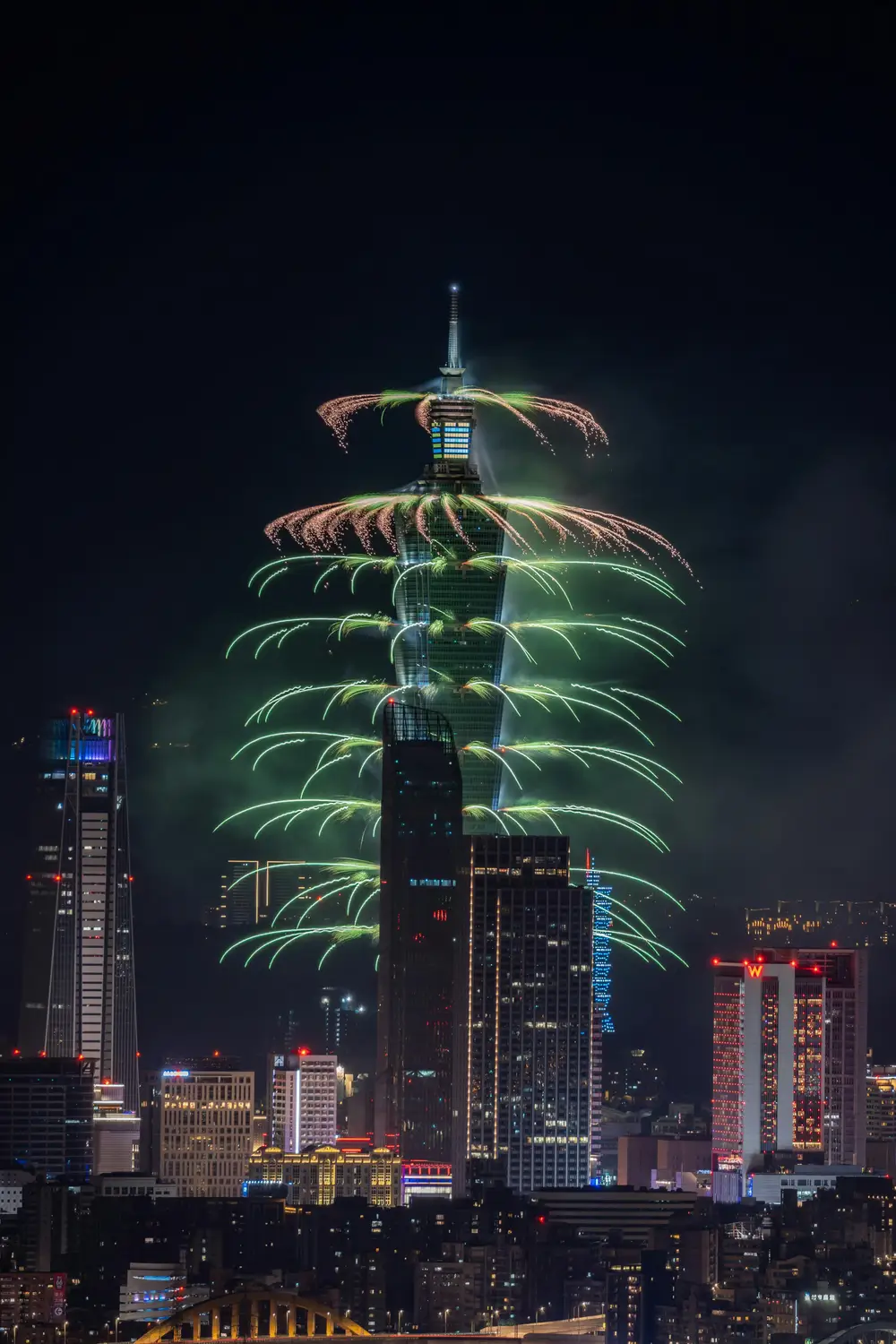 New Year fireworks bursting in green and gold from Taipei 101 skyscraper against the night Taipei skyline