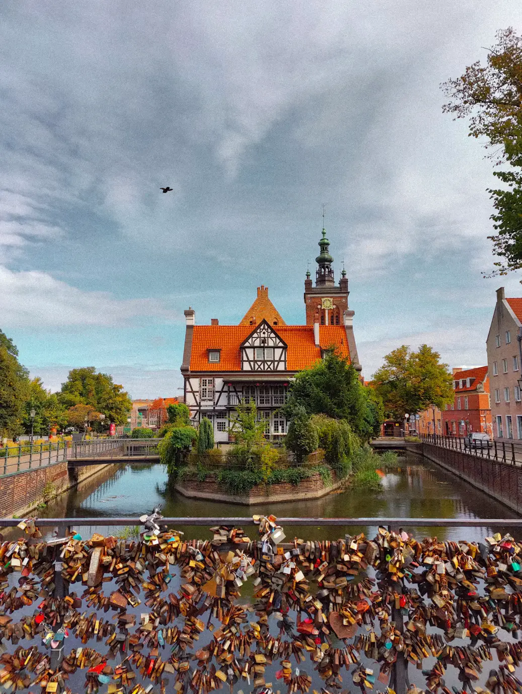 Colorful historic Polish buildings along a waterfront canal, with boats and reflections under a cloudy sky
