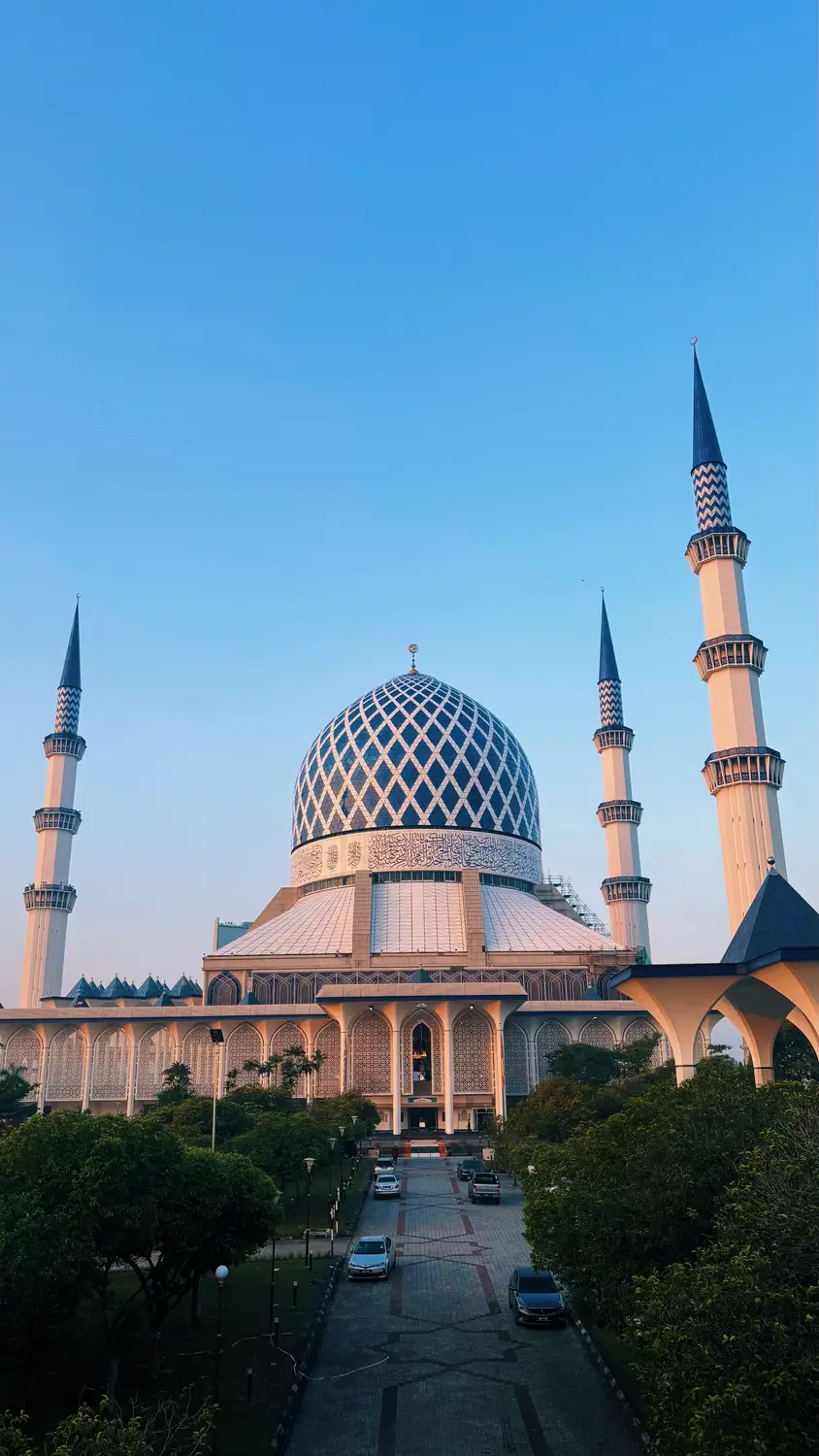 Sultan Salahuddin Abdul Aziz Shah Mosque with large blue silver dome and four minarets against clear blue sky in Shah Alam Selangor Malaysia