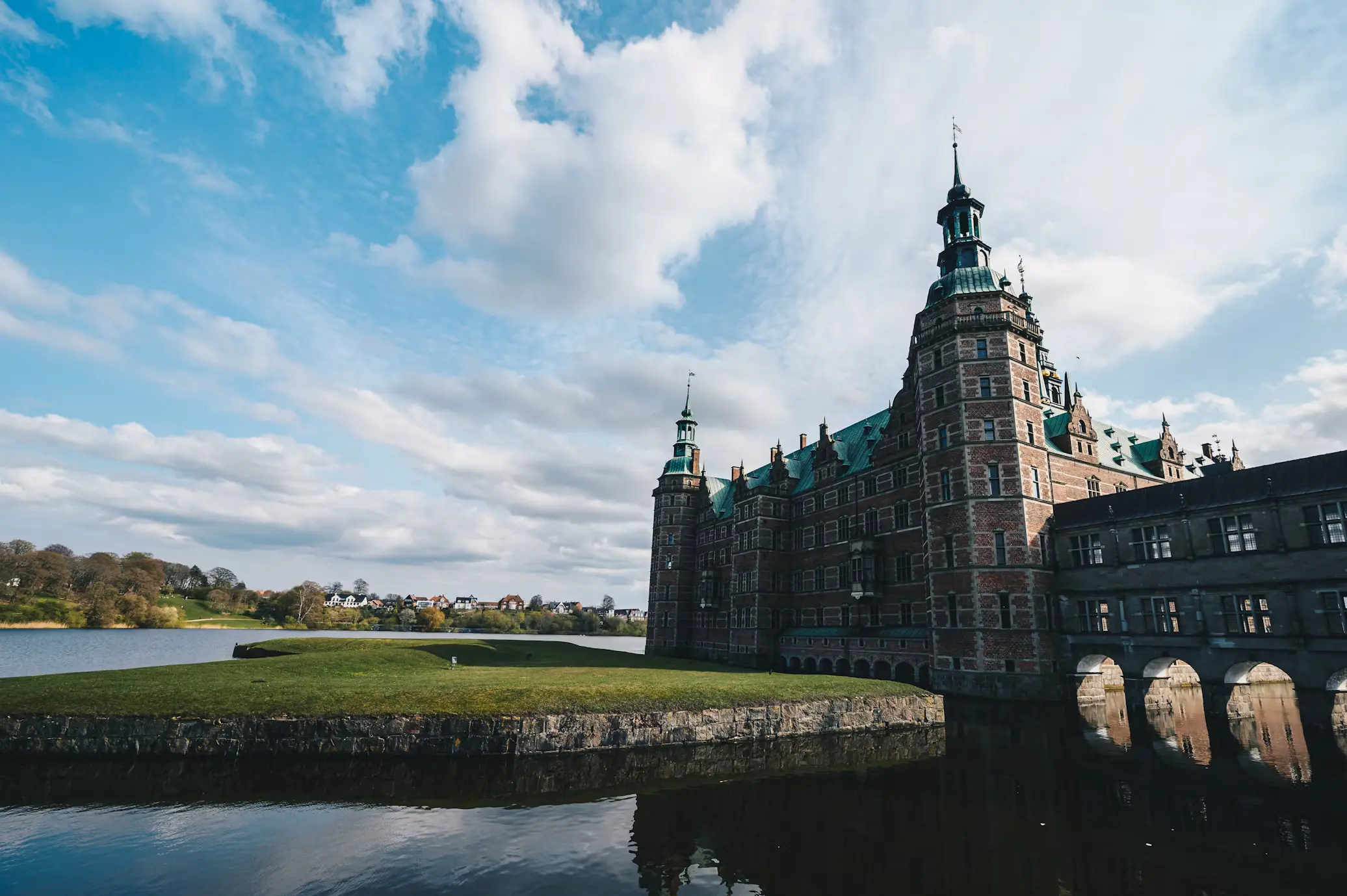Frederiksborg Castle in Denmark reflected in its moat, with towers rising against a blue sky
