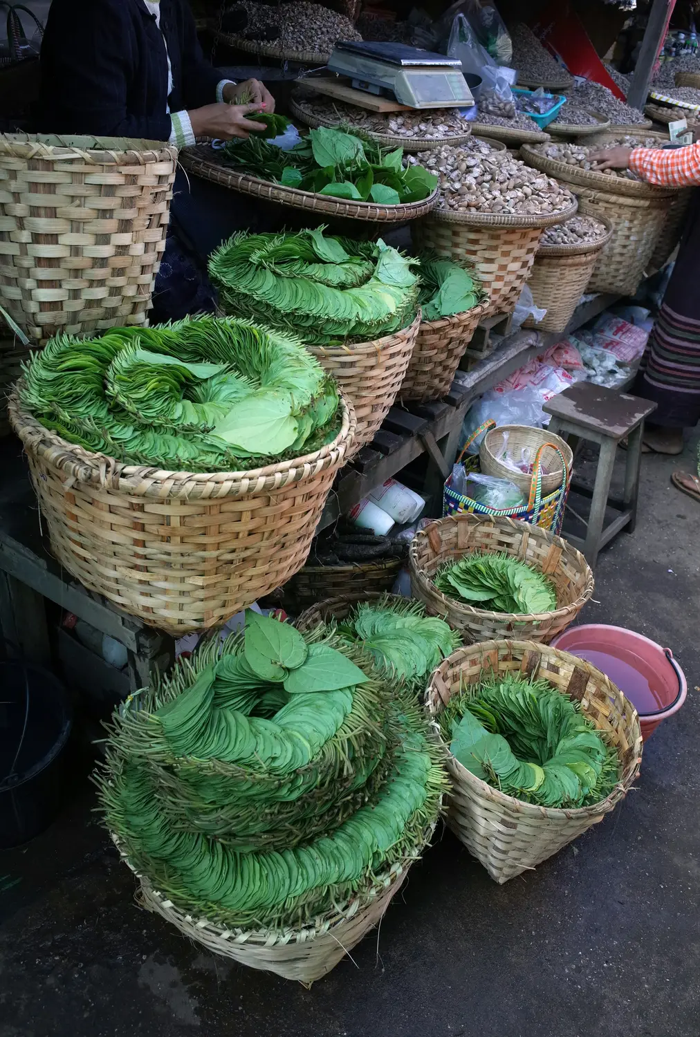 Fresh betel leaves and dried nuts arranged in woven bamboo baskets at traditional Myanmar street market stall
