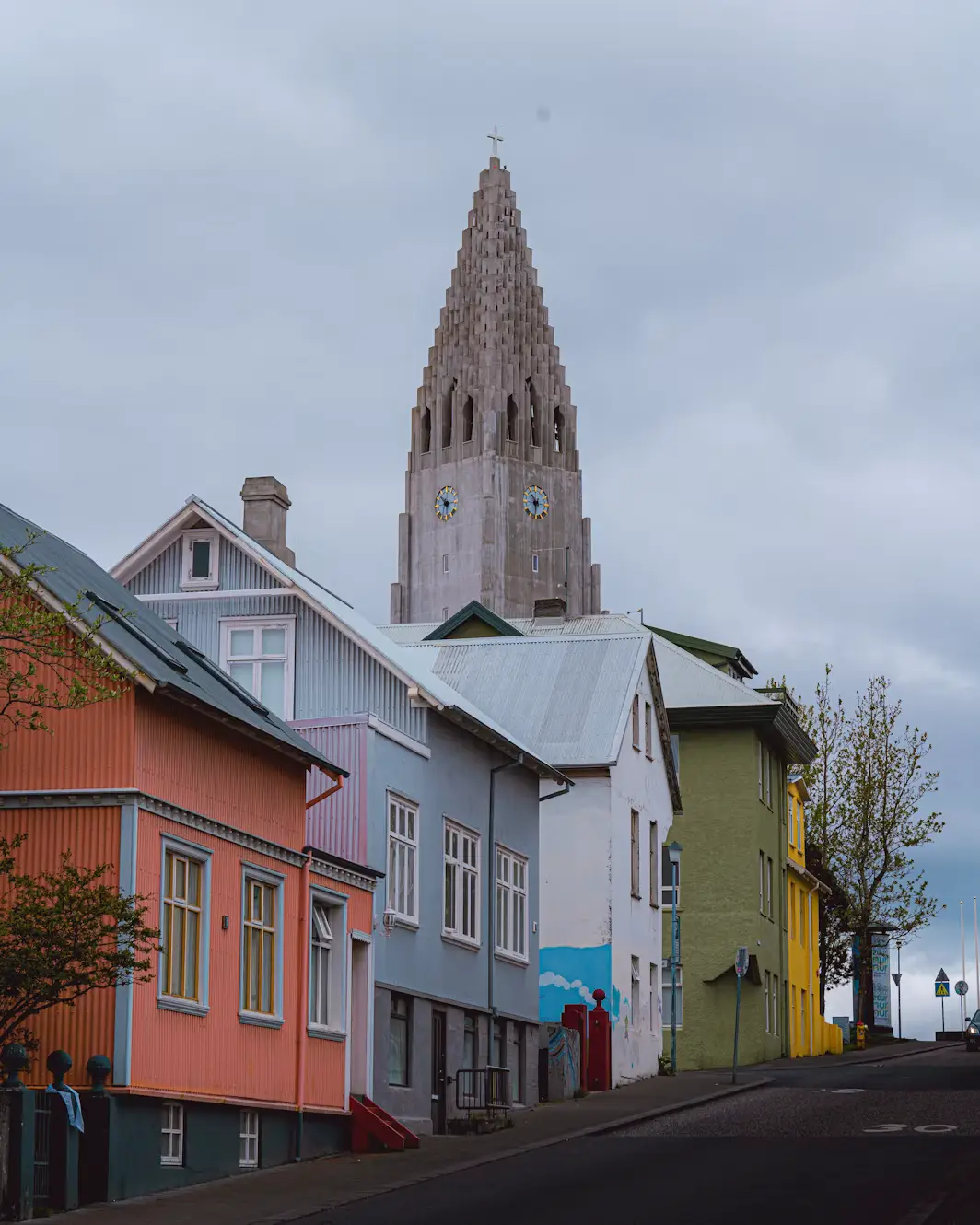 Row of colorful houses lining a street, with a tall church spire rising behind them, Iceland.