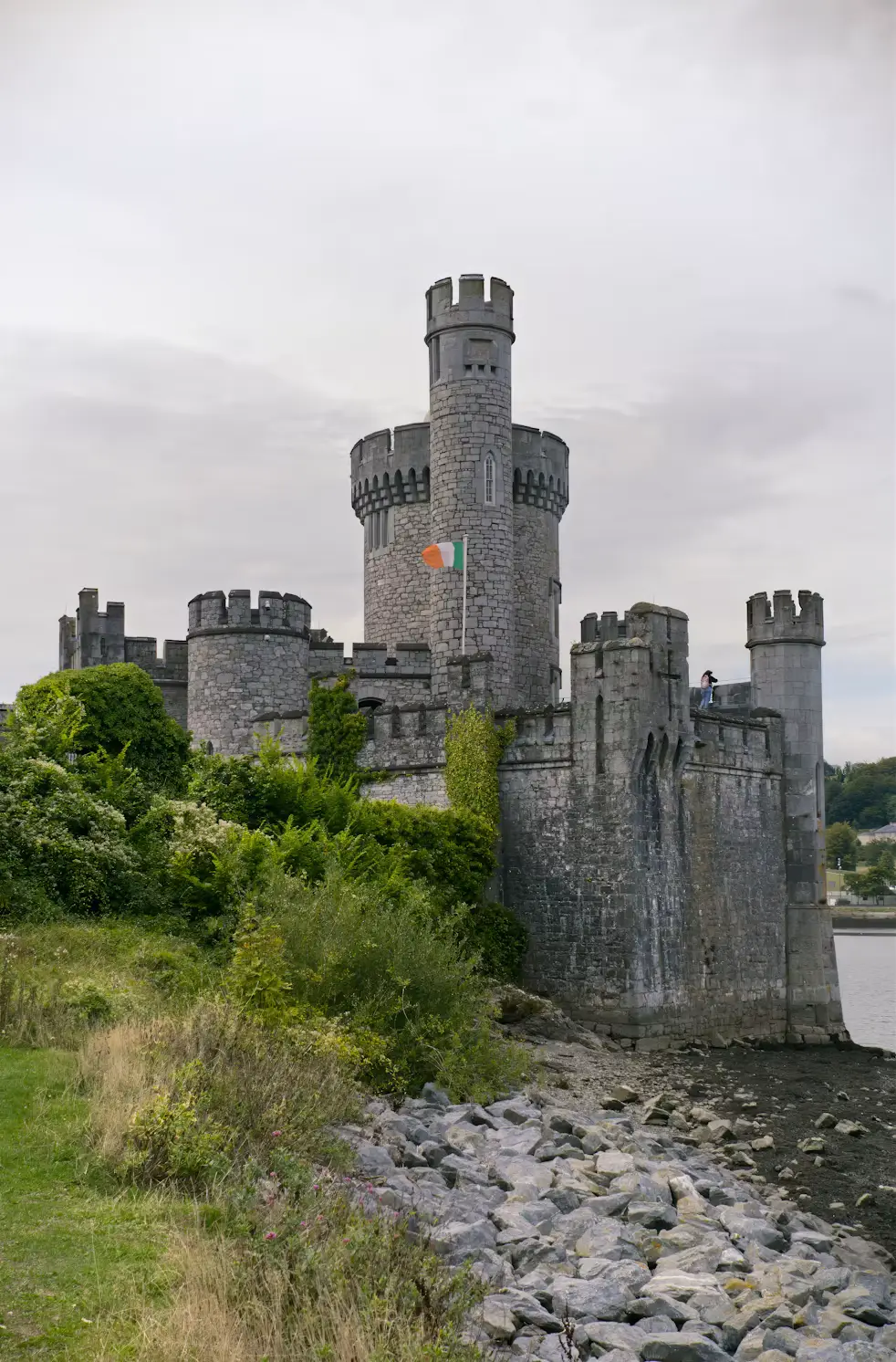 Stone castle with turreted towers beside a rocky riverbank, Ireland.