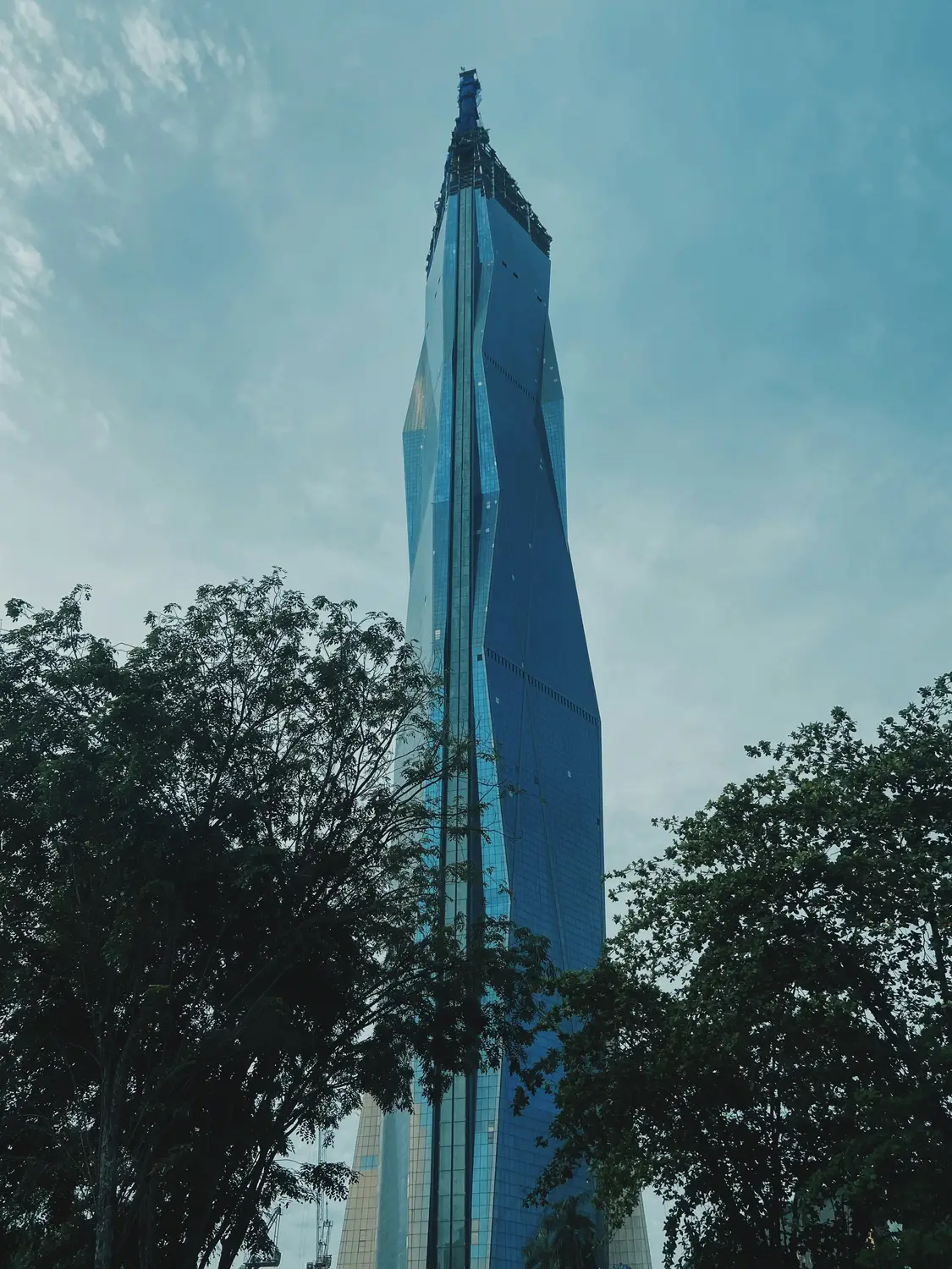 Low angle upward view of modern glass facade skyscraper tower reflecting blue sky and trees in Kuala Lumpur Malaysia