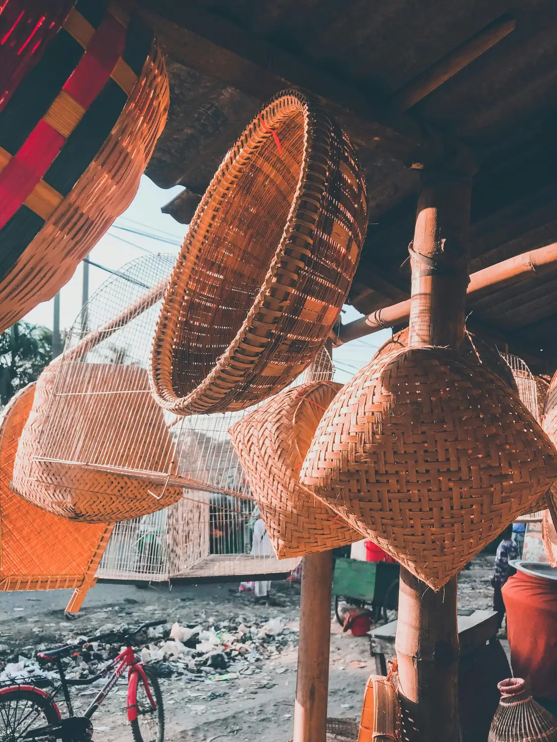 Handwoven bamboo fish traps and wicker baskets hanging for sale at a rural market in Bangladesh