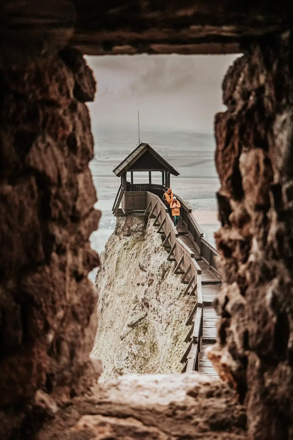 Wooden lookout and walkway on a rocky cliff viewed through a stone opening.