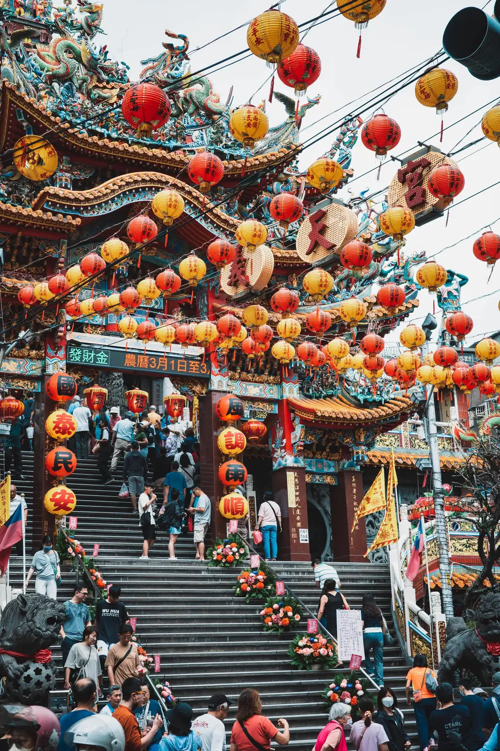 Crowds climbing the steps of a Taiwanese temple draped with hundreds of red and yellow paper lanterns during a festival
