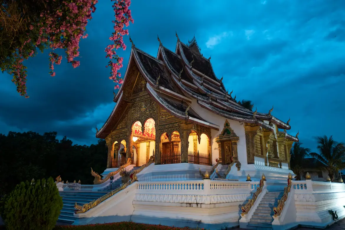 Illuminated golden Buddhist temple with ornate Lao architecture at dusk in Luang Prabang, Laos.