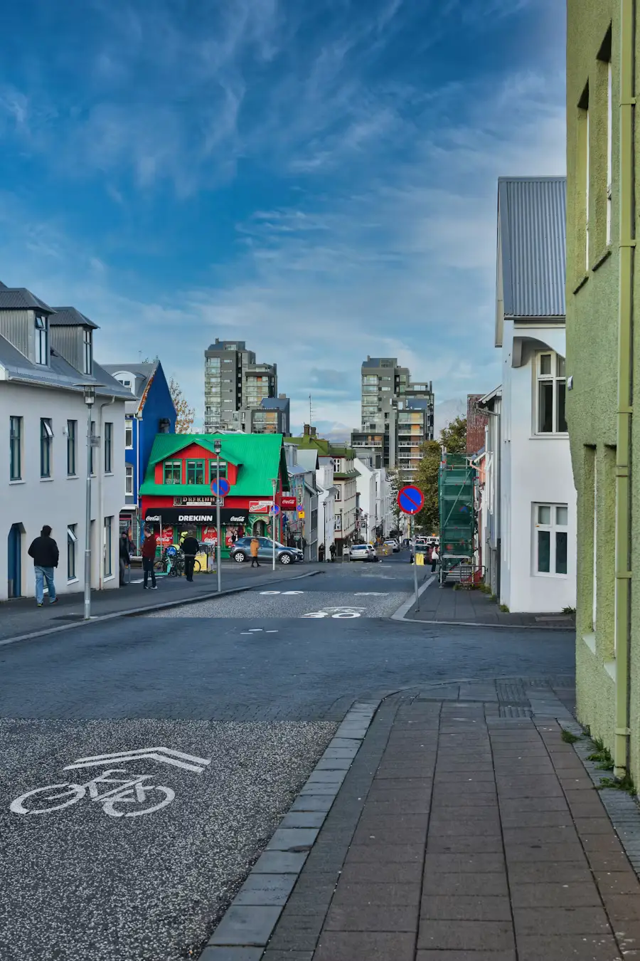 City street lined with colorful low-rise buildings and a bike lane, under a partly cloudy sky, Reykjavík, Iceland.