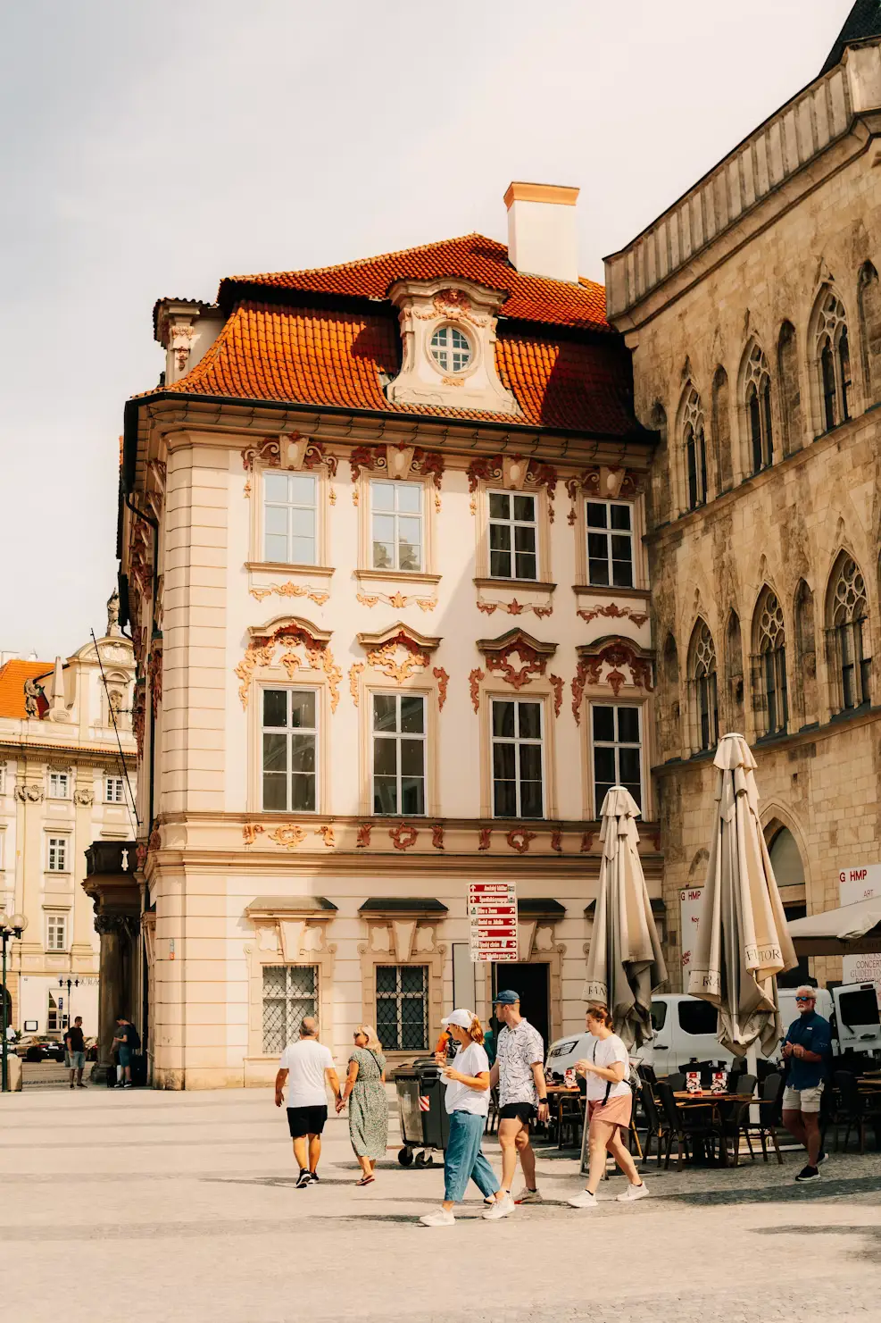 People walking and dining outdoors in front of a baroque building in a Prague square