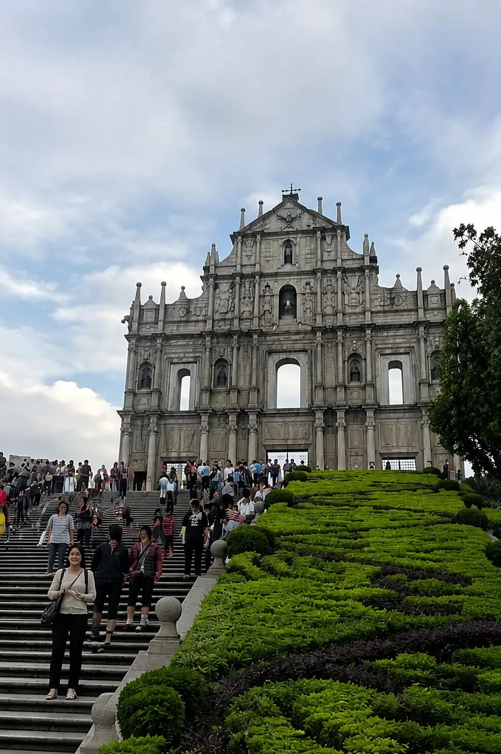 Ruins of St. Paul's viewed from staircase with tourists and manicured garden