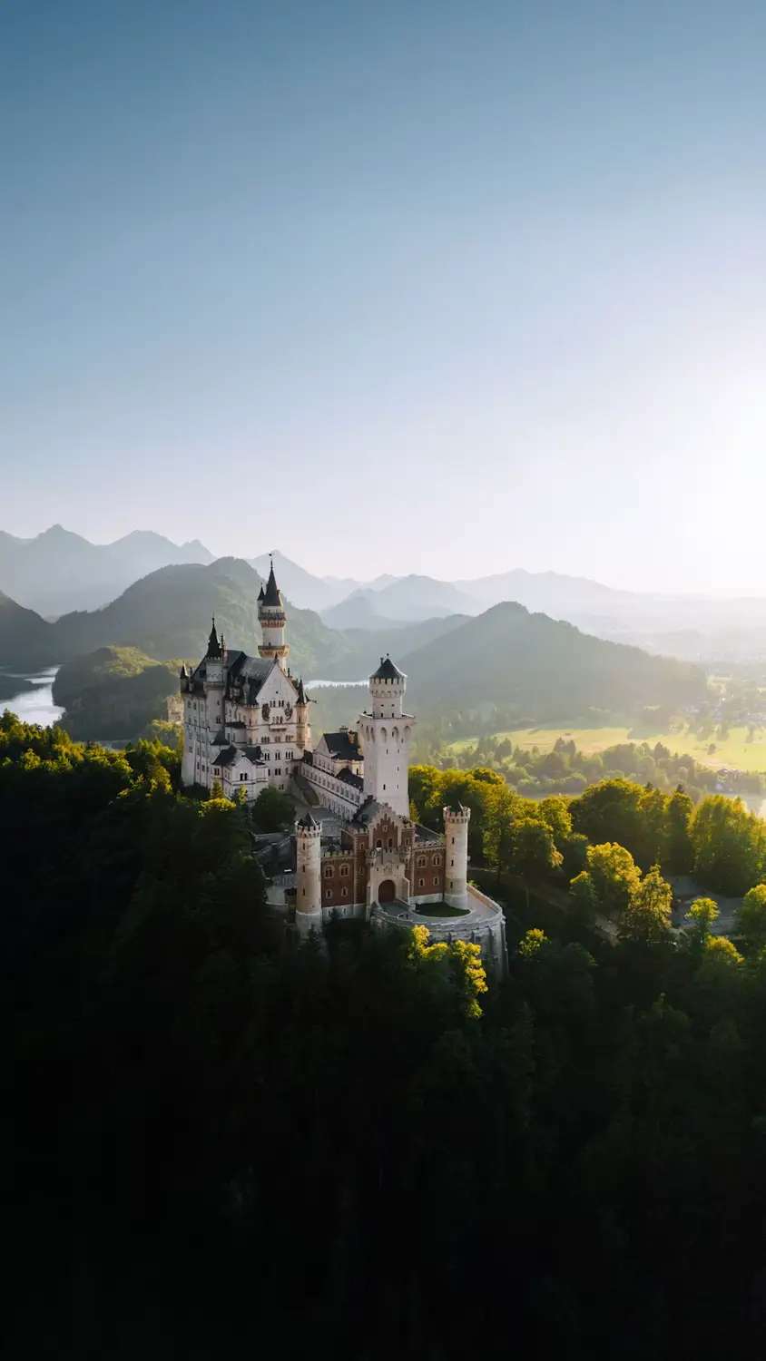 Neuschwanstein Castle at sunrise with misty mountains in the background