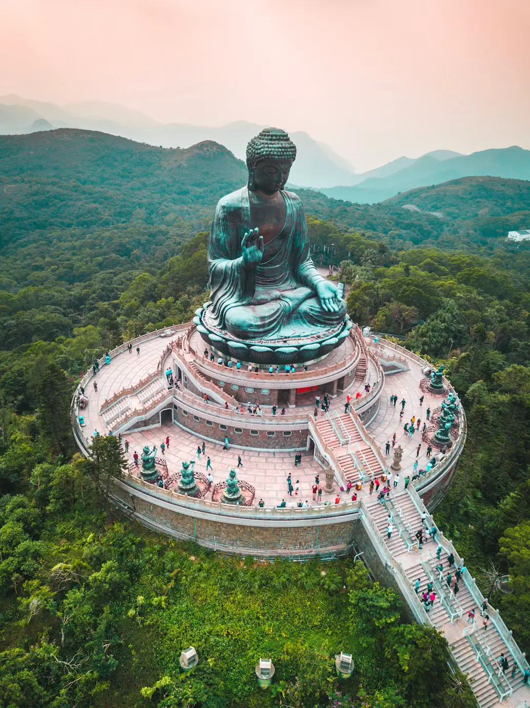 Aerial view of the Tian Tan Big Buddha statue surrounded by forested mountains on Lantau Island in Hong Kong.
