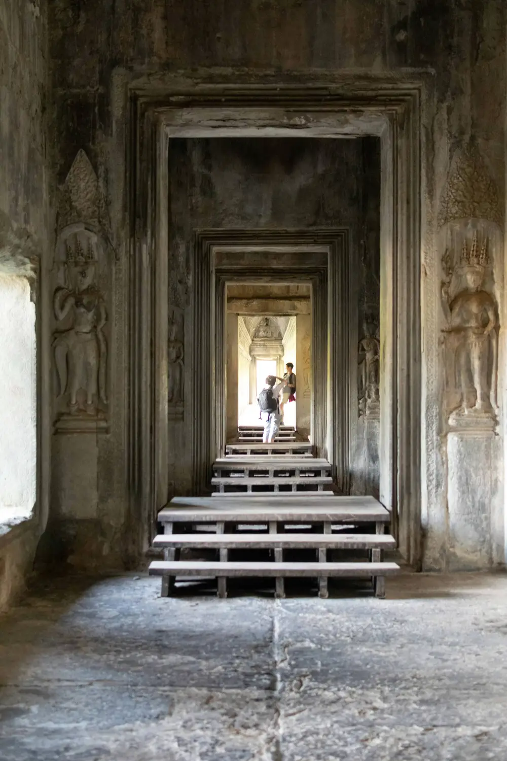 Long perspective corridor with multiple stone doorways and Apsara relief carvings inside Angkor Wat temple, Siem Reap, Cambodia
