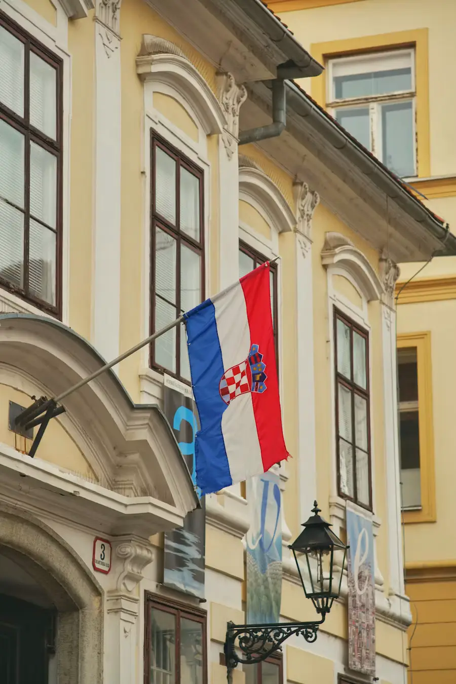 Croatian flag hanging from a yellow historic building with ornate windows.