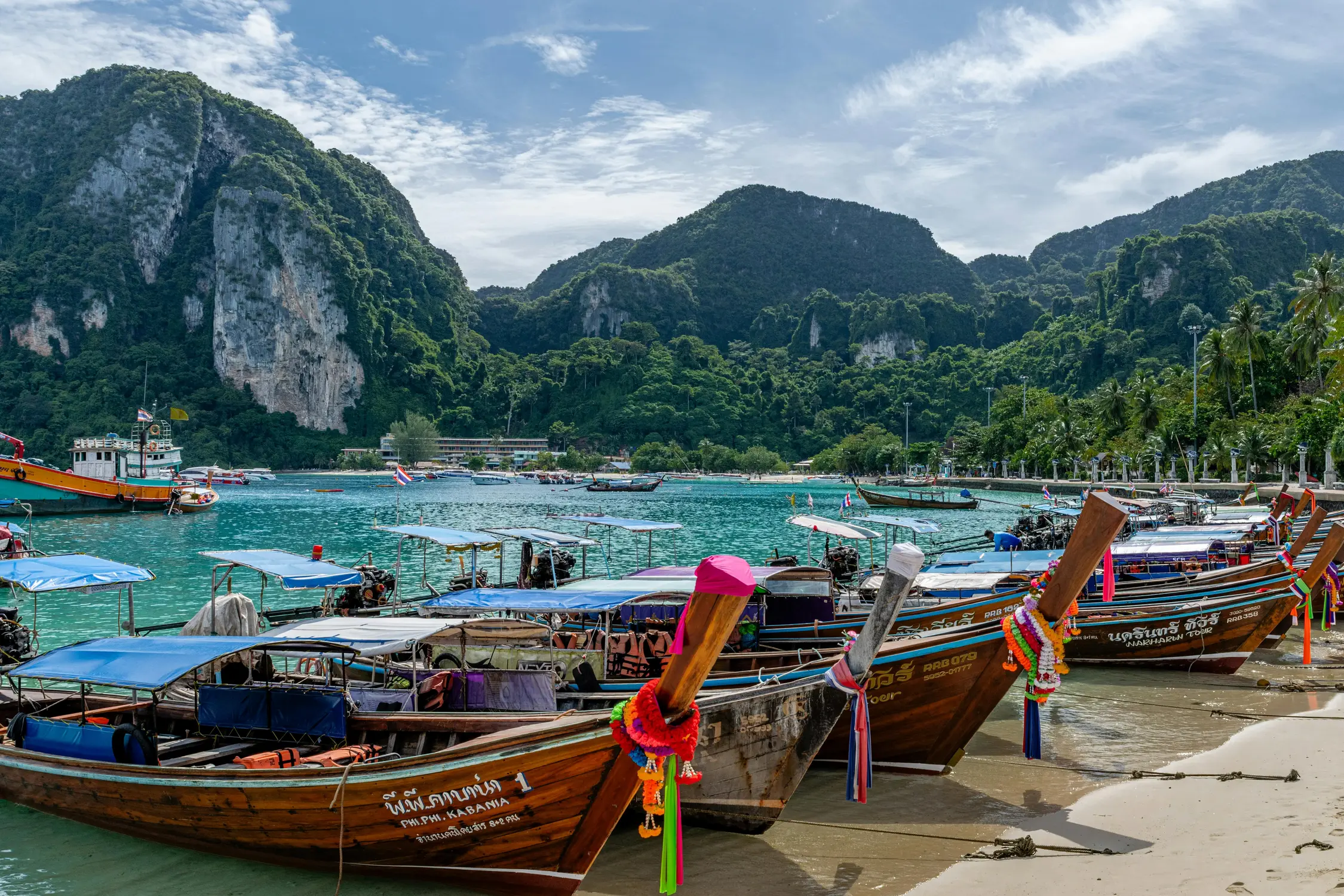 Colourful wooden longtail boats moored along the beach at Phi Phi Island, Thailand, with turquoise water and limestone karst mountains in the background