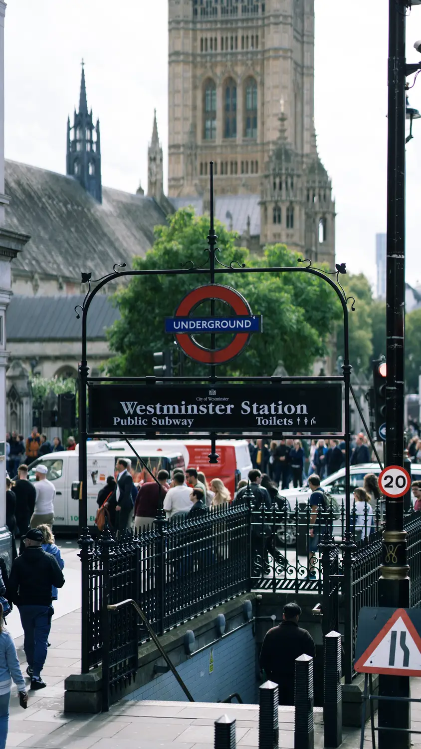 Entrance to Westminster Underground station with its roundel sign, and the towers of the Houses of Parliament rising behind.