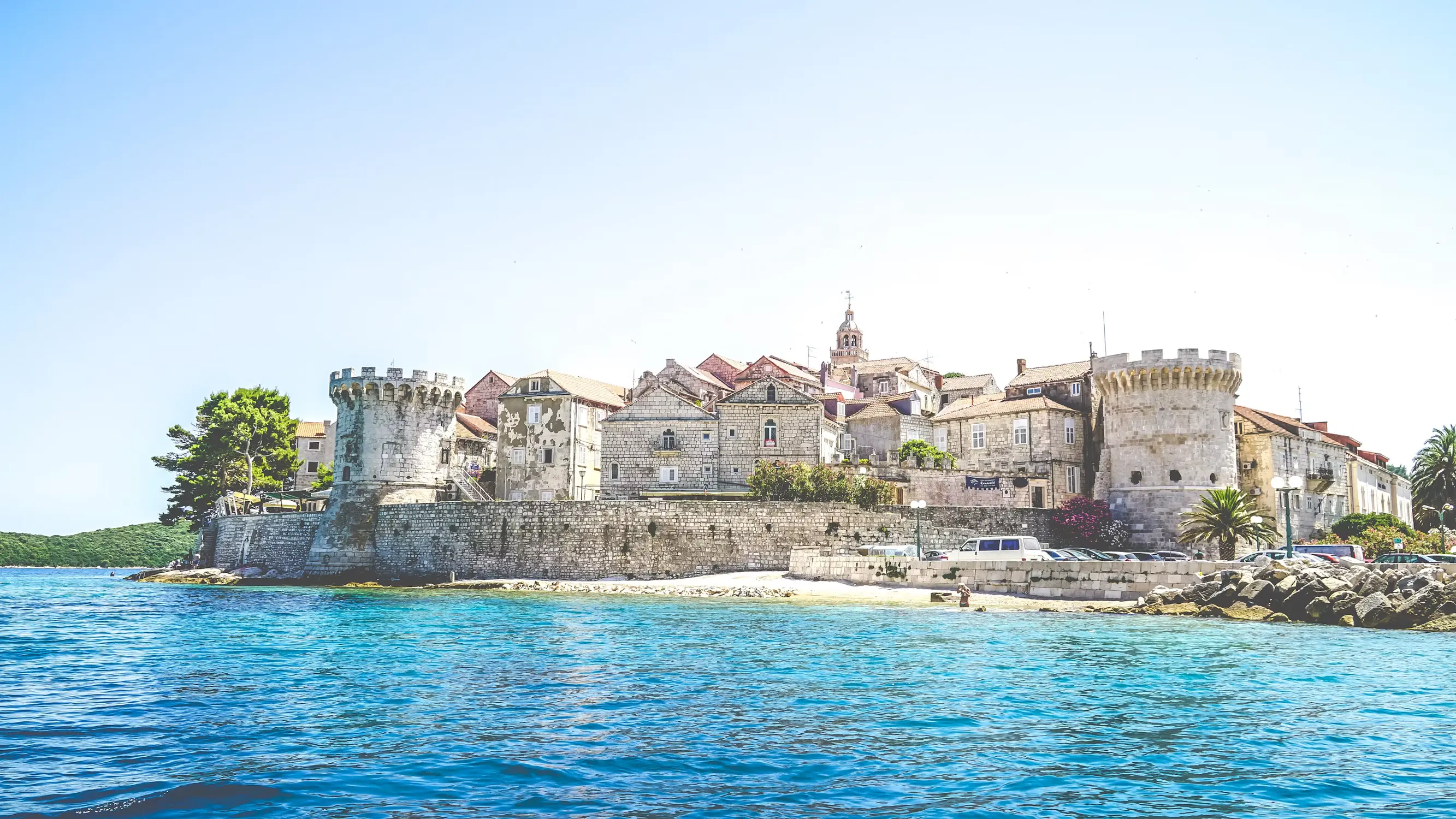 Medieval walled town of Korčula on a small peninsula, with a stone fortress and red-roofed buildings surrounded by turquoise sea, Croatia.