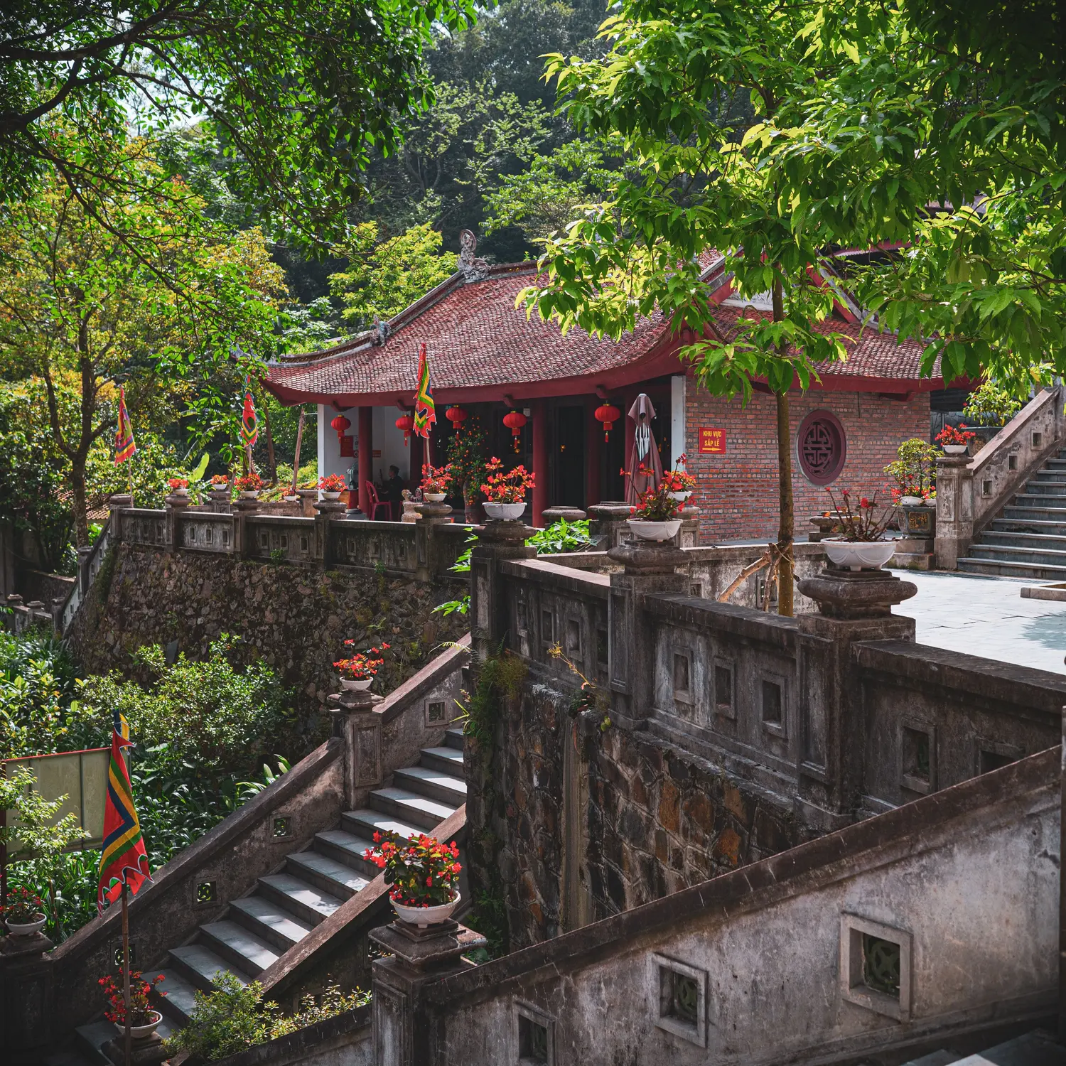 Red-roofed temple pavilion above stone stairways amid green trees.