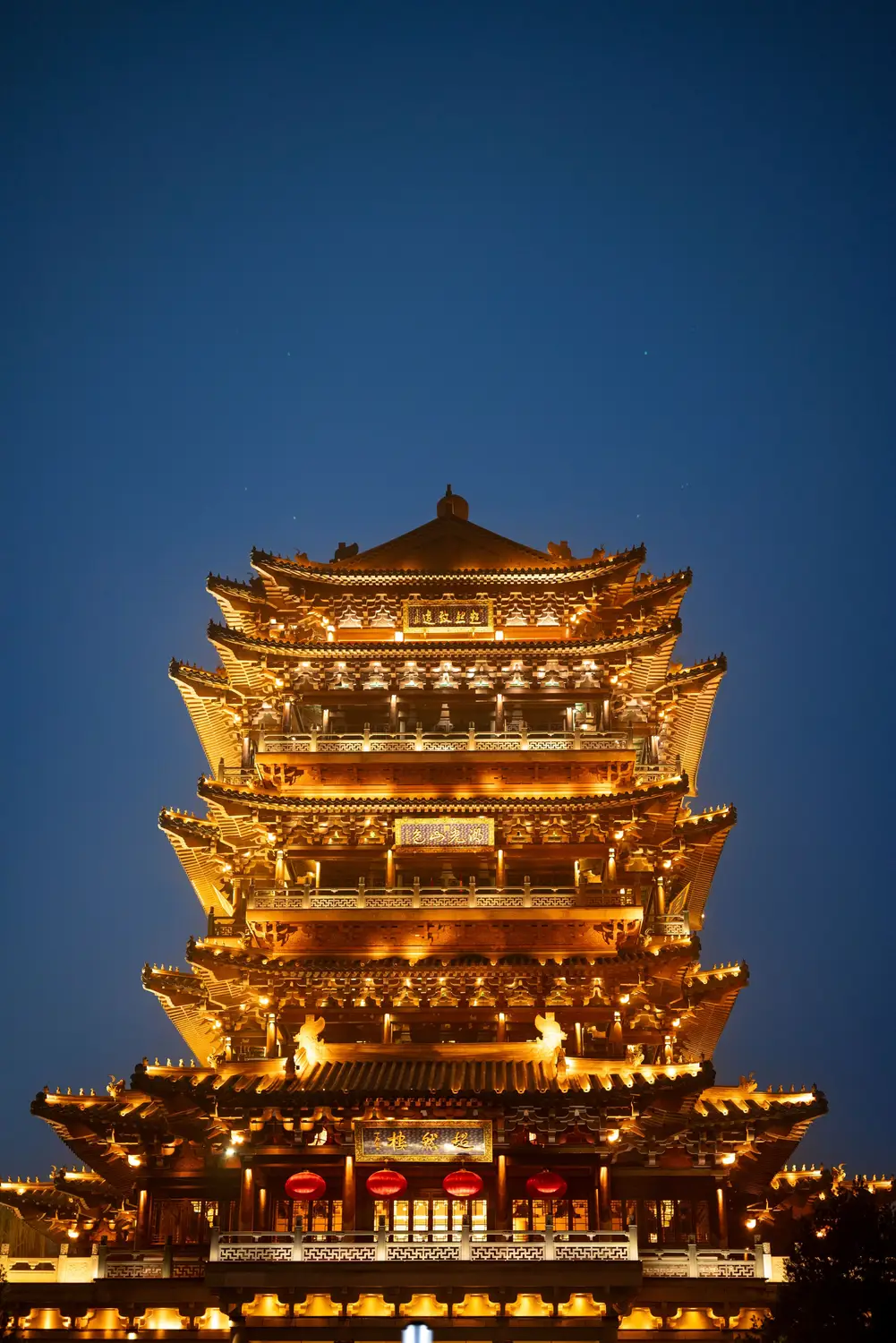 Ancient Chinese multi-story tower pagoda dramatically illuminated in golden light against deep blue night sky