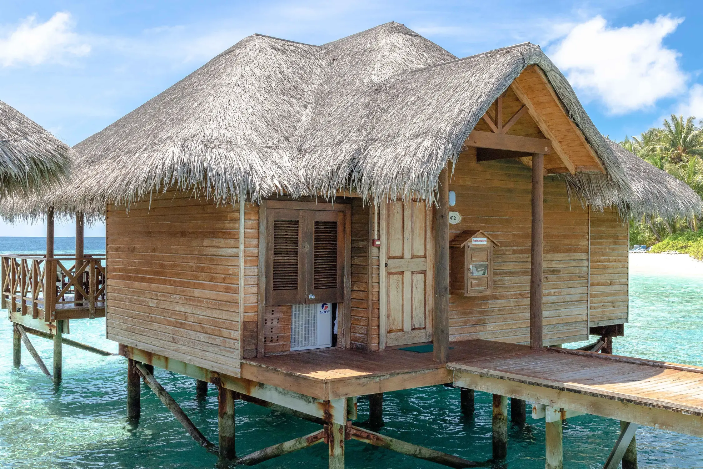 Wooden overwater bungalow with thatched roof and private deck over turquoise clear ocean water at Maldives island resort