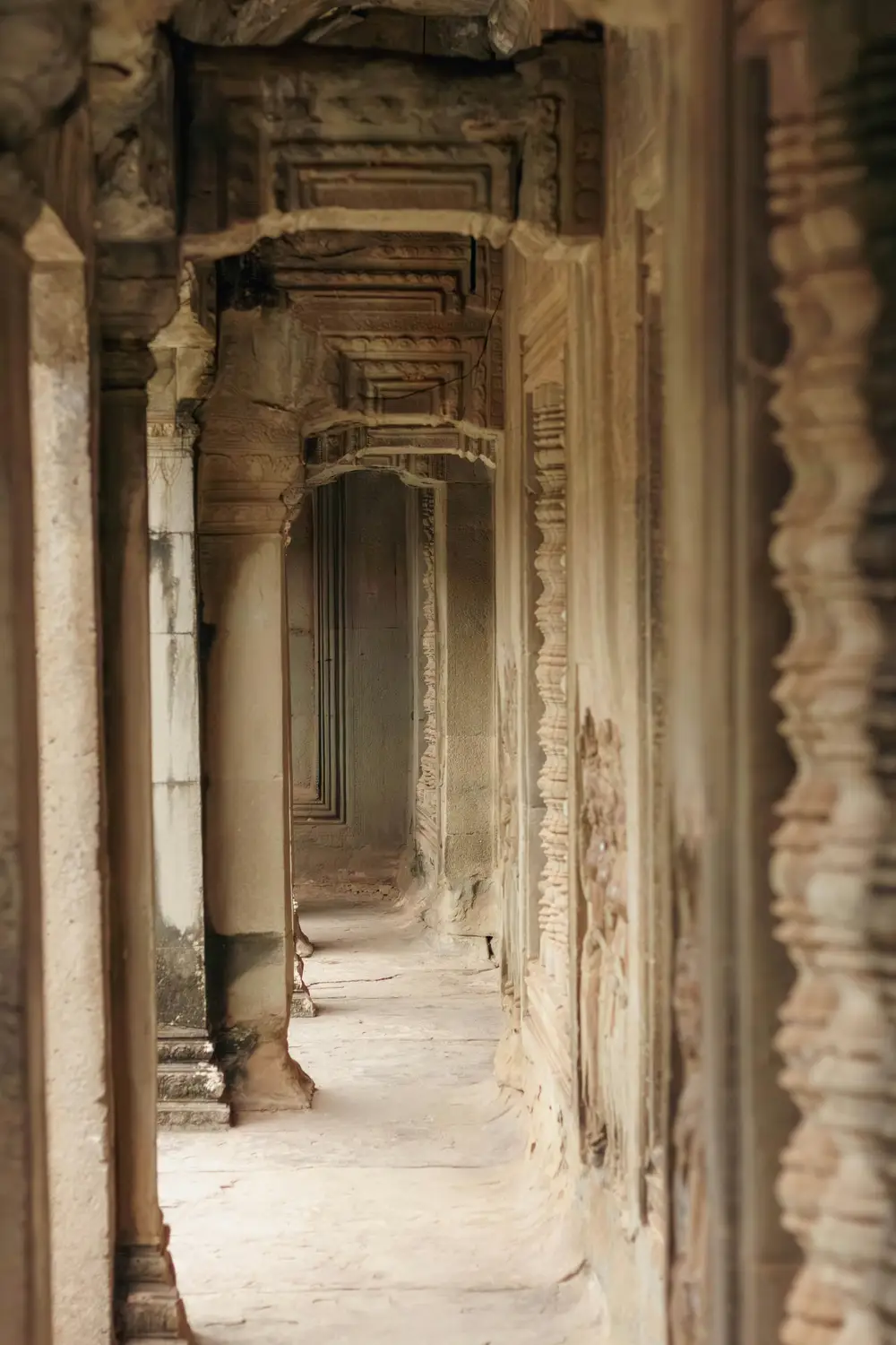 Ancient stone corridor with arched doorways and intricate carved columns inside Angkor Wat temple, Siem Reap, Cambodia