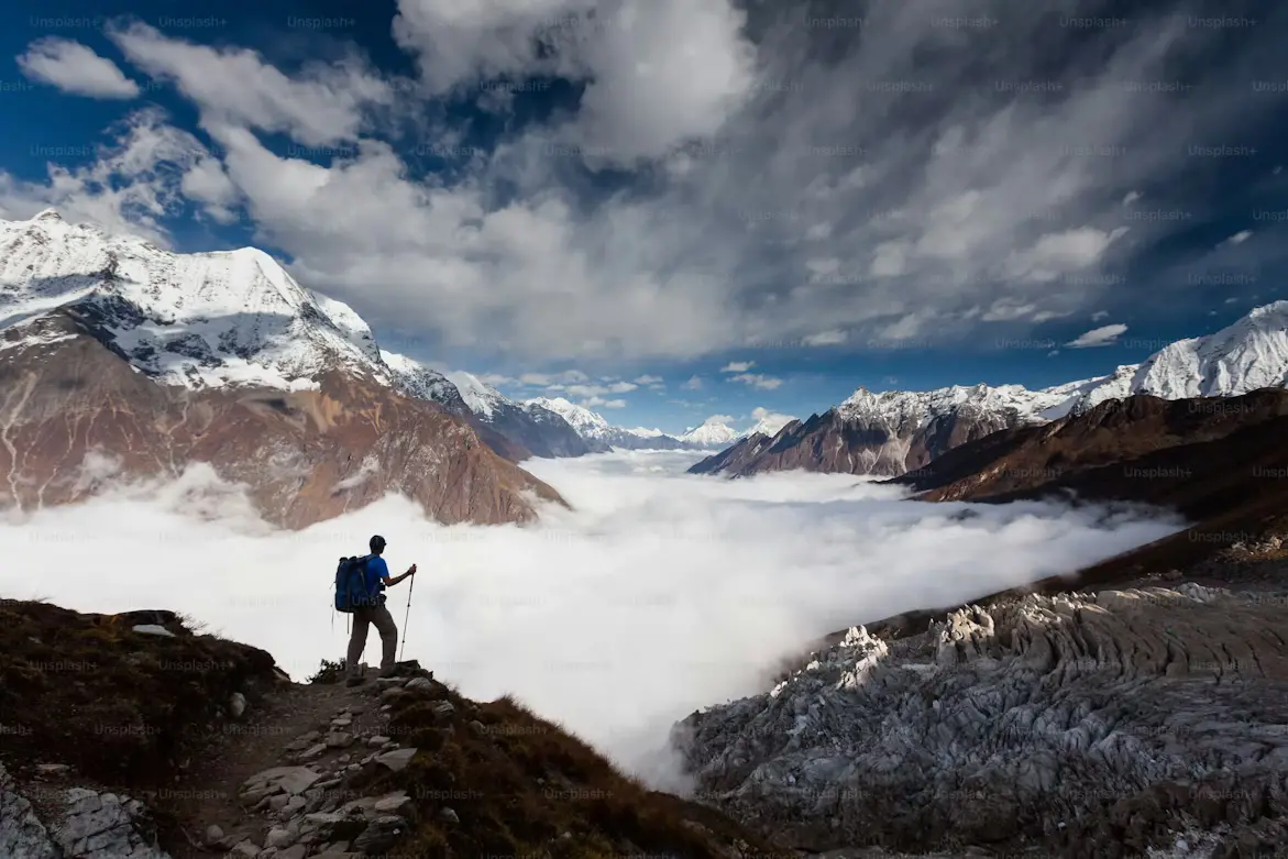 Hiker with backpack standing on a rocky ridge overlooking a cloud-filled valley in the Nepal Himalayas