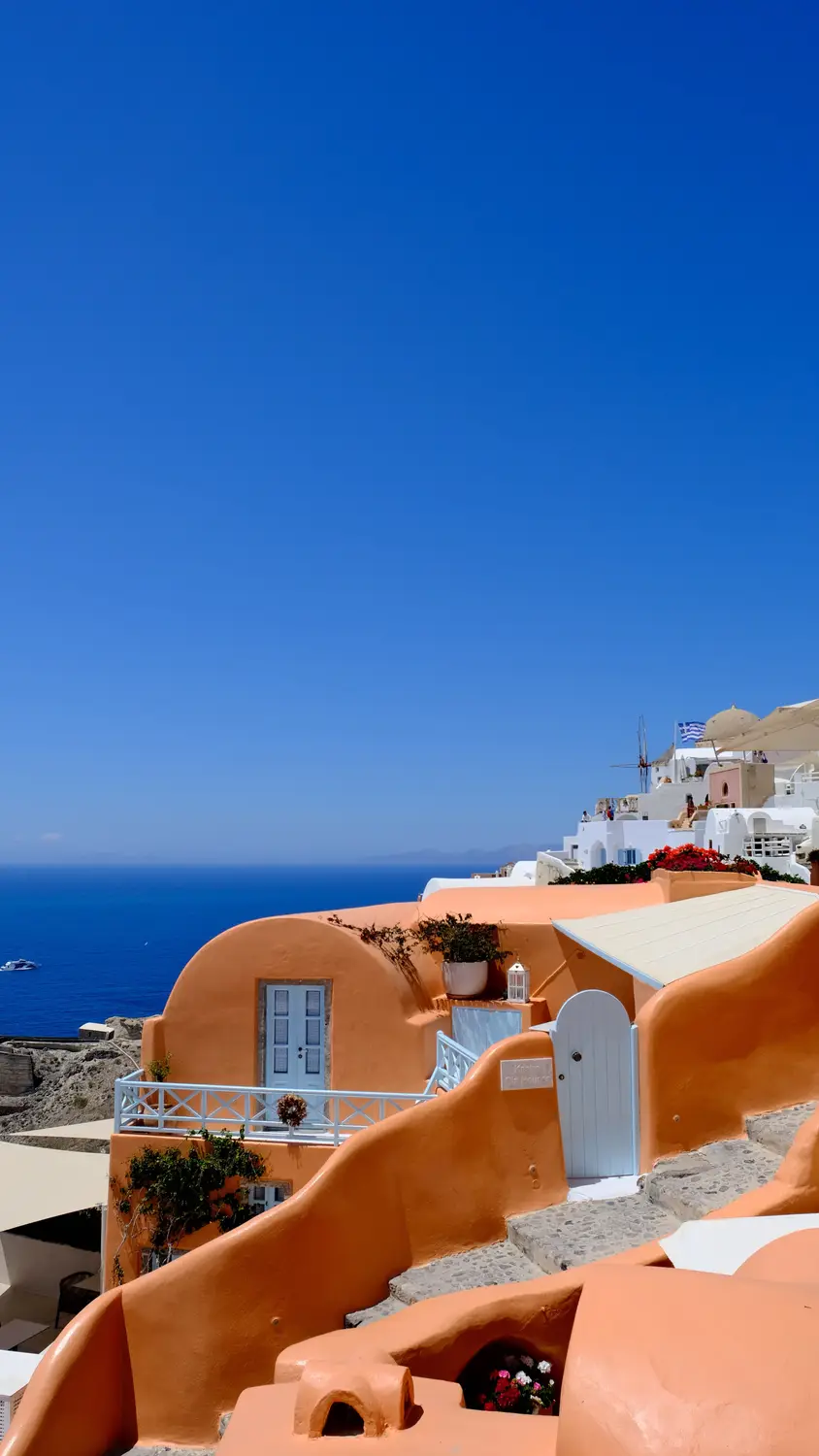 Terracotta-domed buildings in Santorini overlooking the deep blue sea, set against a clear sky.