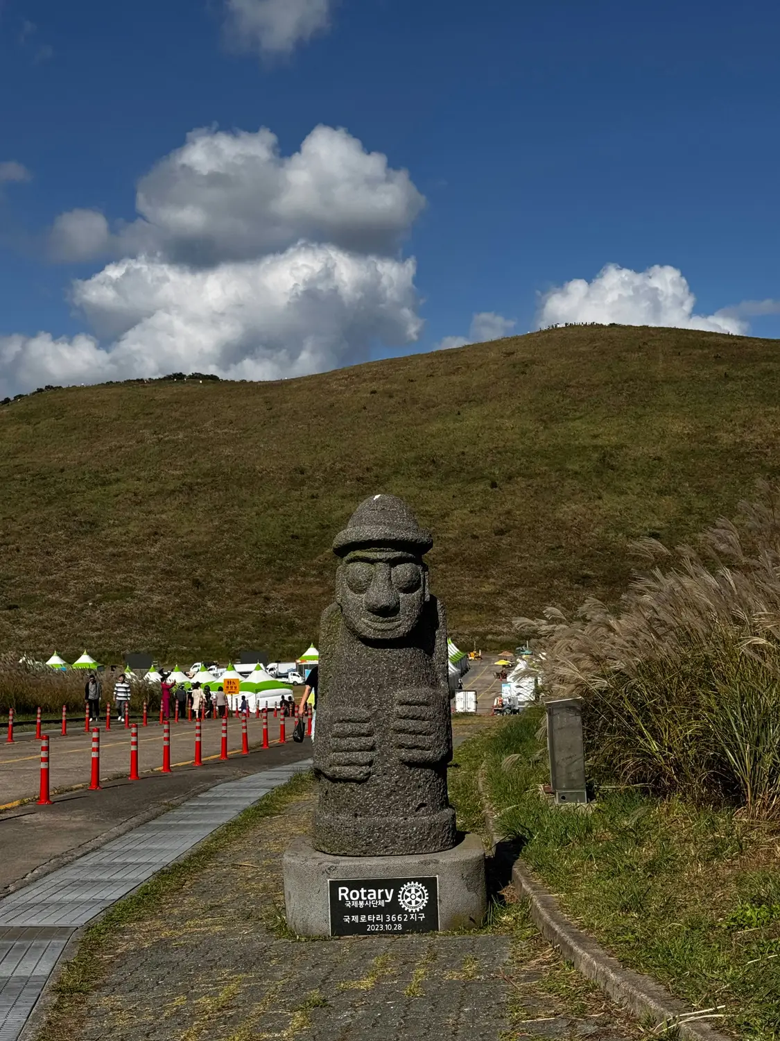 Stone dol hareubang grandfather statue on a grassy hillside under a blue sky on Jeju Island, South Korea.