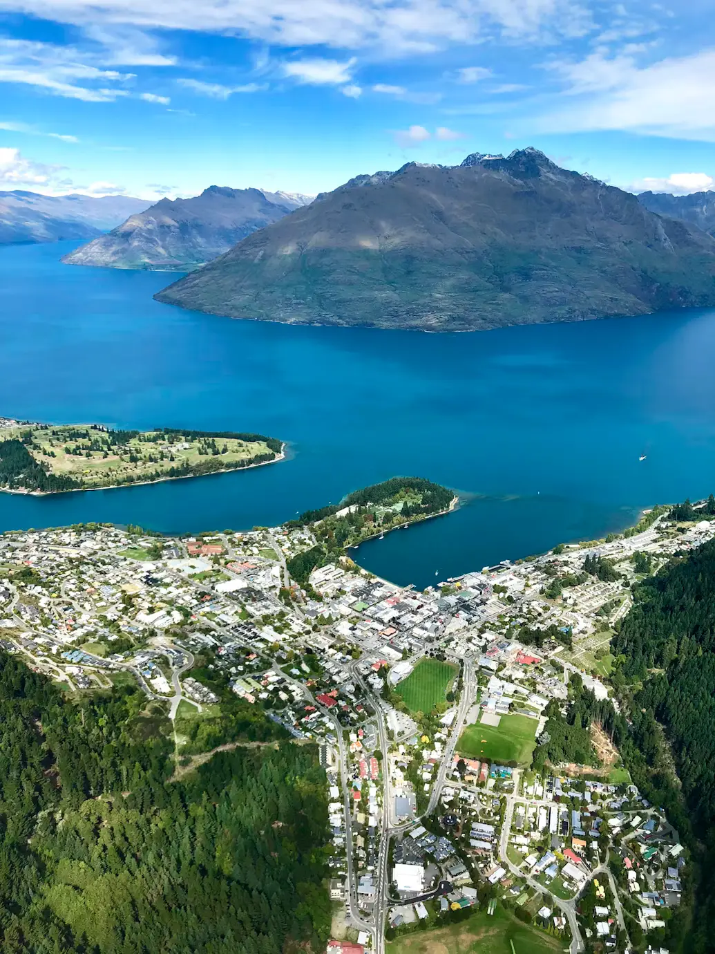 Aerial view of Queenstown beside Lake Wakatipu with surrounding mountains.