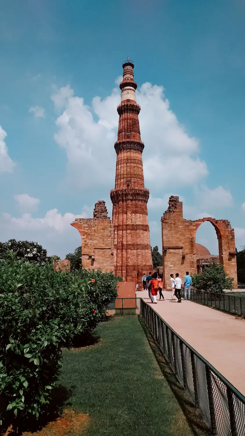 Qutub Minar tall red sandstone UNESCO minaret with ruins and tourists on walkway, New Delhi, India