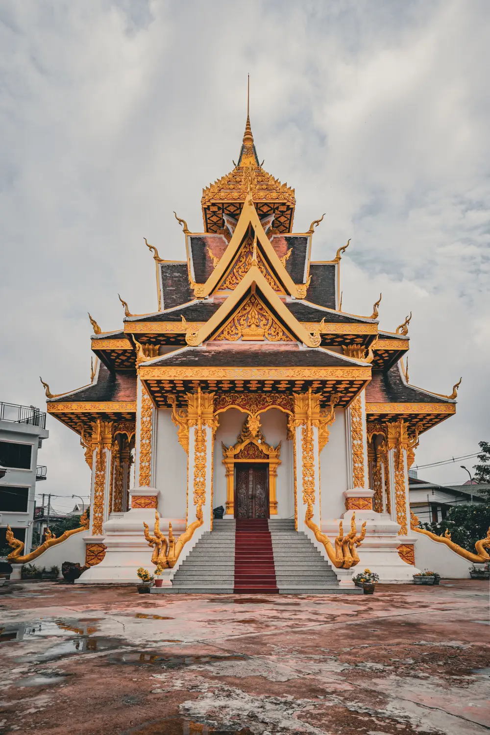 Ornate golden Buddhist temple with a tiered spire under a dramatic cloudy sky in Laos.