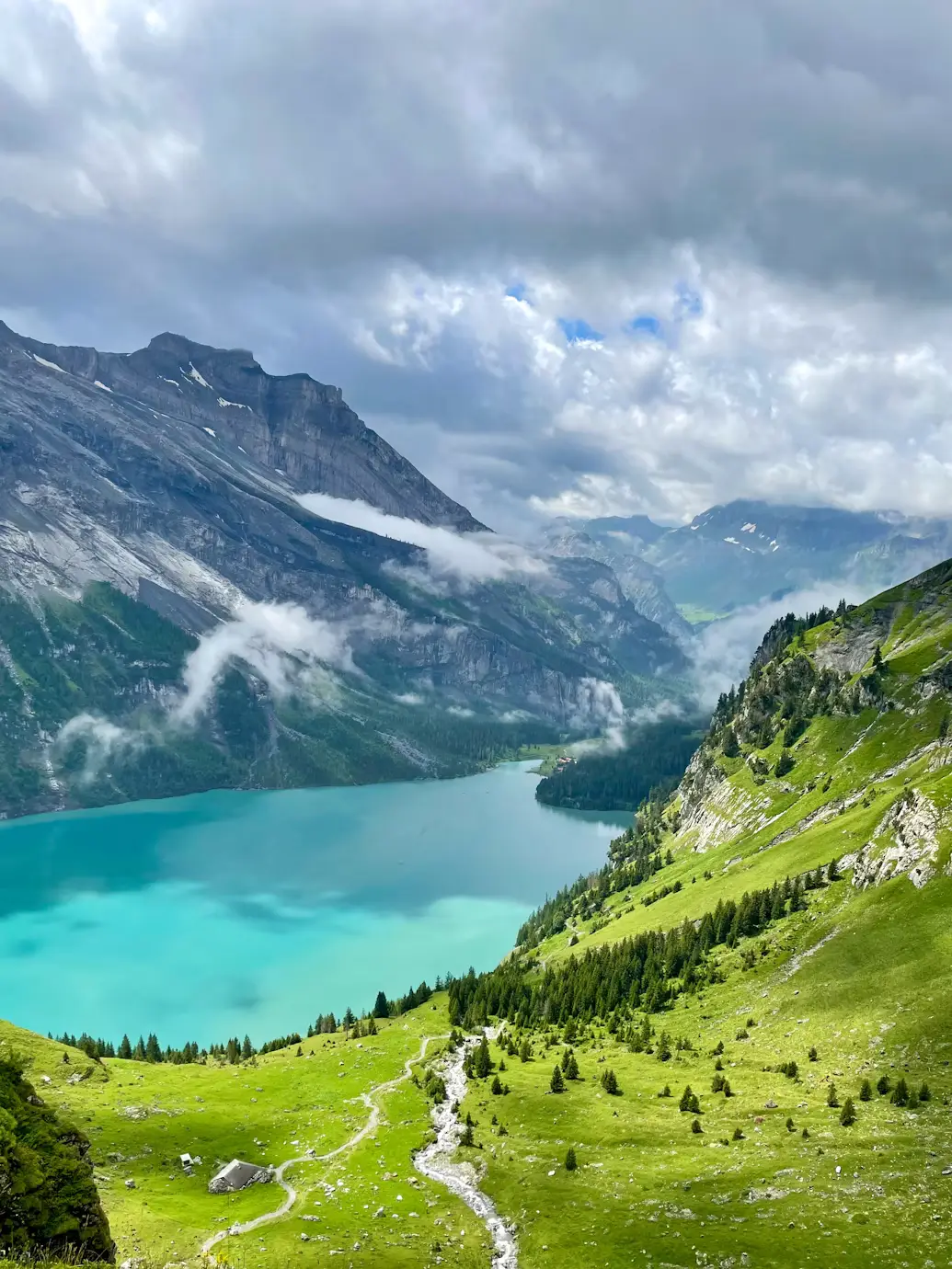 Turquoise glacial lake surrounded by green hills and misty mountains, Switzerland
