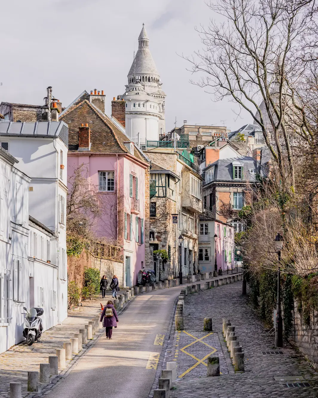 Cobblestone street in Montmartre lined with pastel buildings and the Sacré-Cœur dome in the distance