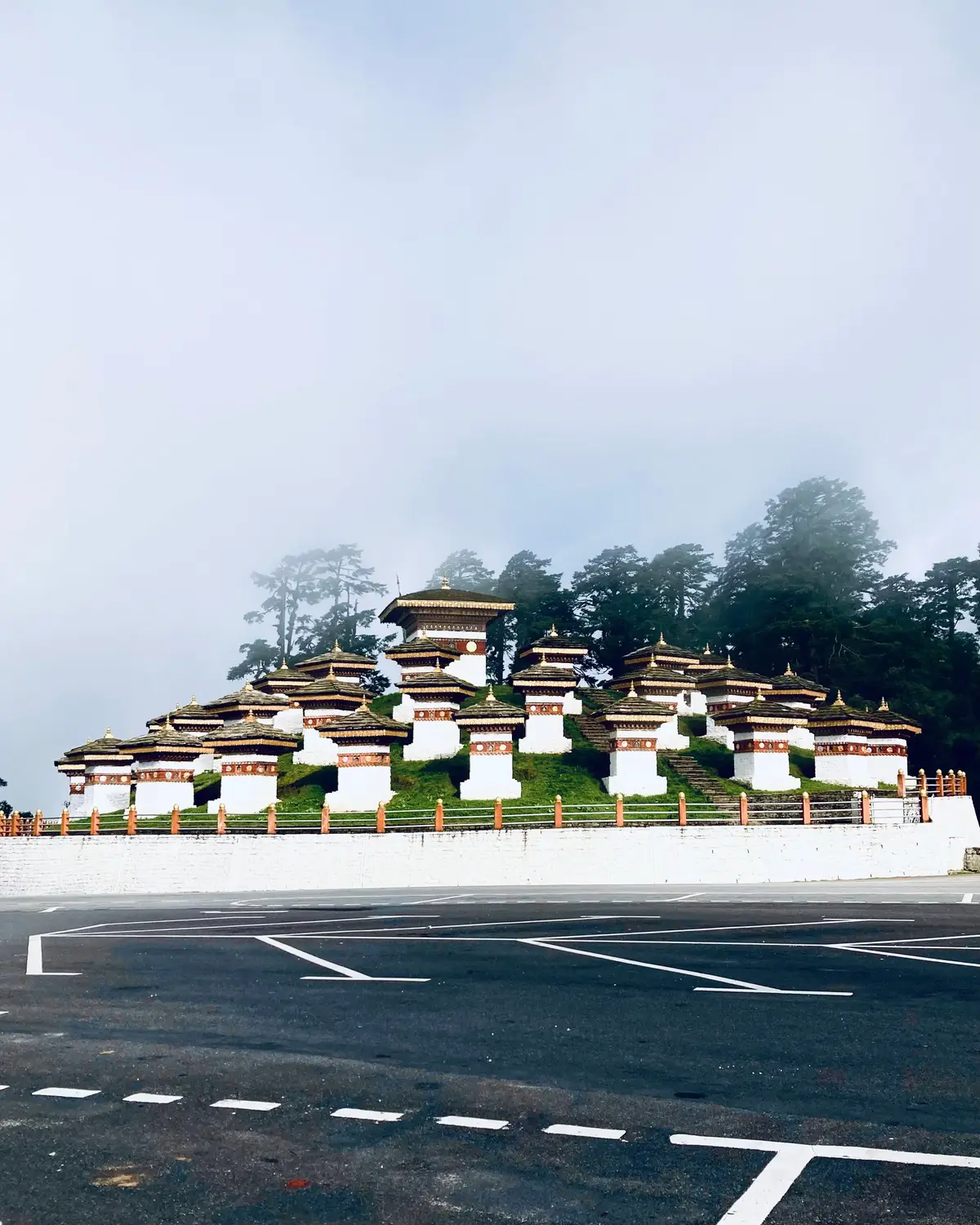 Row of 108 memorial chortens (Druk Wangyal Chortens) on a misty hilltop above an empty mountain road at Dochula Pass in Bhutan.