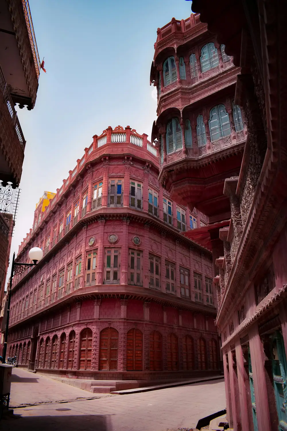Ornate multi-storey pink sandstone haveli with arched balconies on narrow street, Bikaner old city, Rajasthan, India