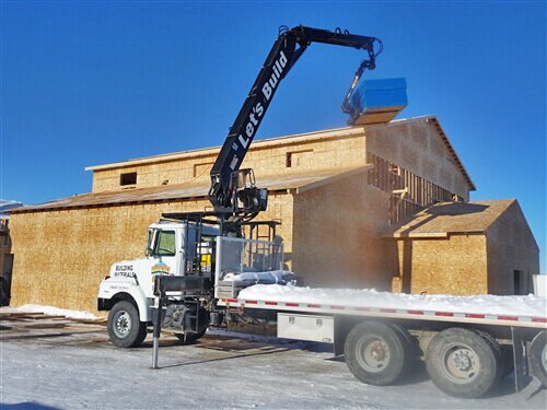 Crane lifting building supplies up to a roof of a framed house structure
