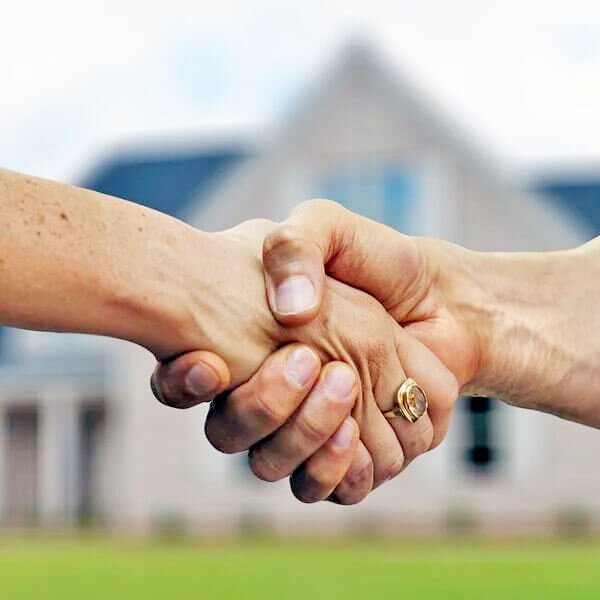 two people's hands shaking in front of a house